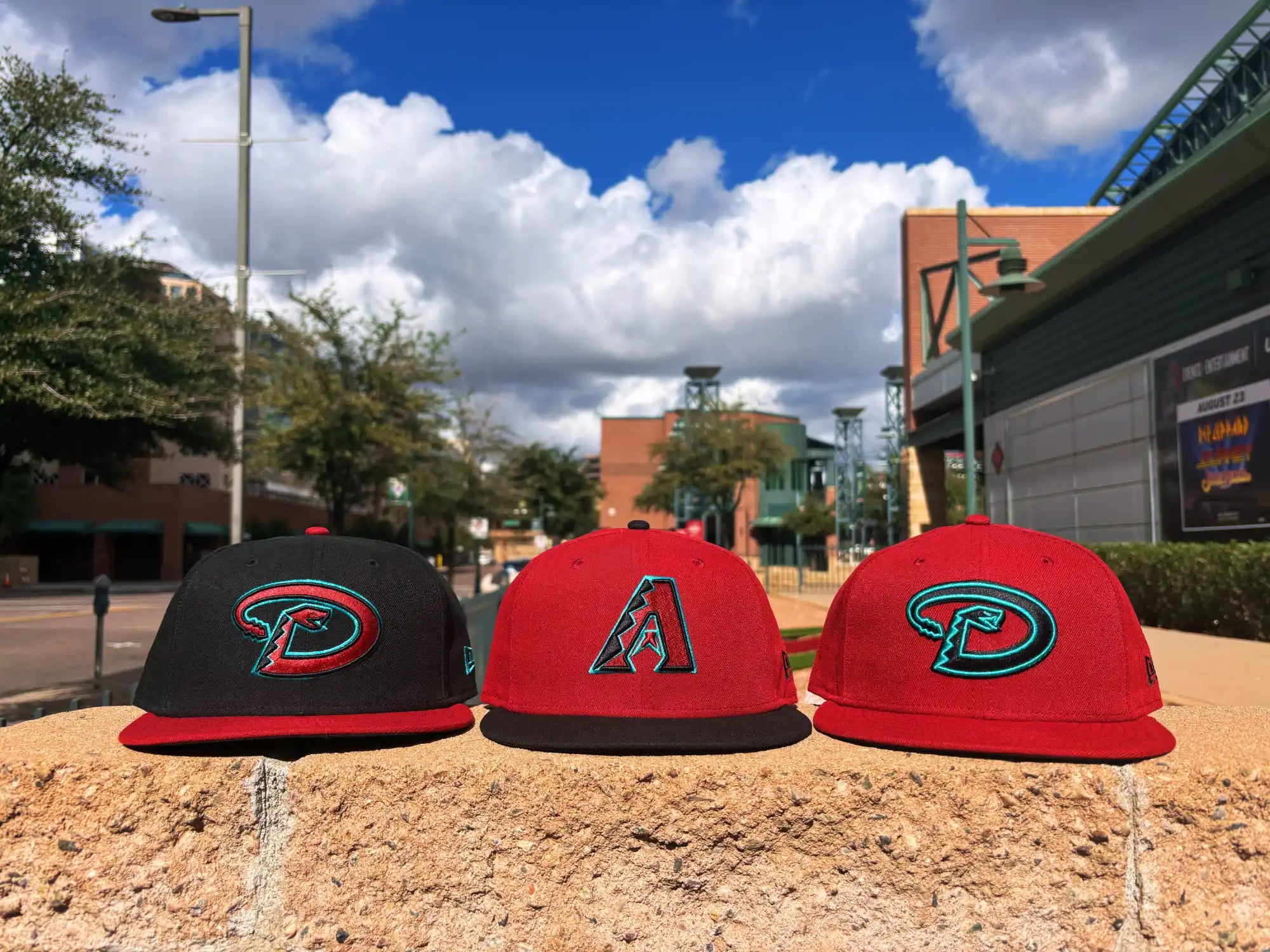 Three baseball caps featuring Arizona Diamondbacks and Portland Pickles logos arranged on sand.