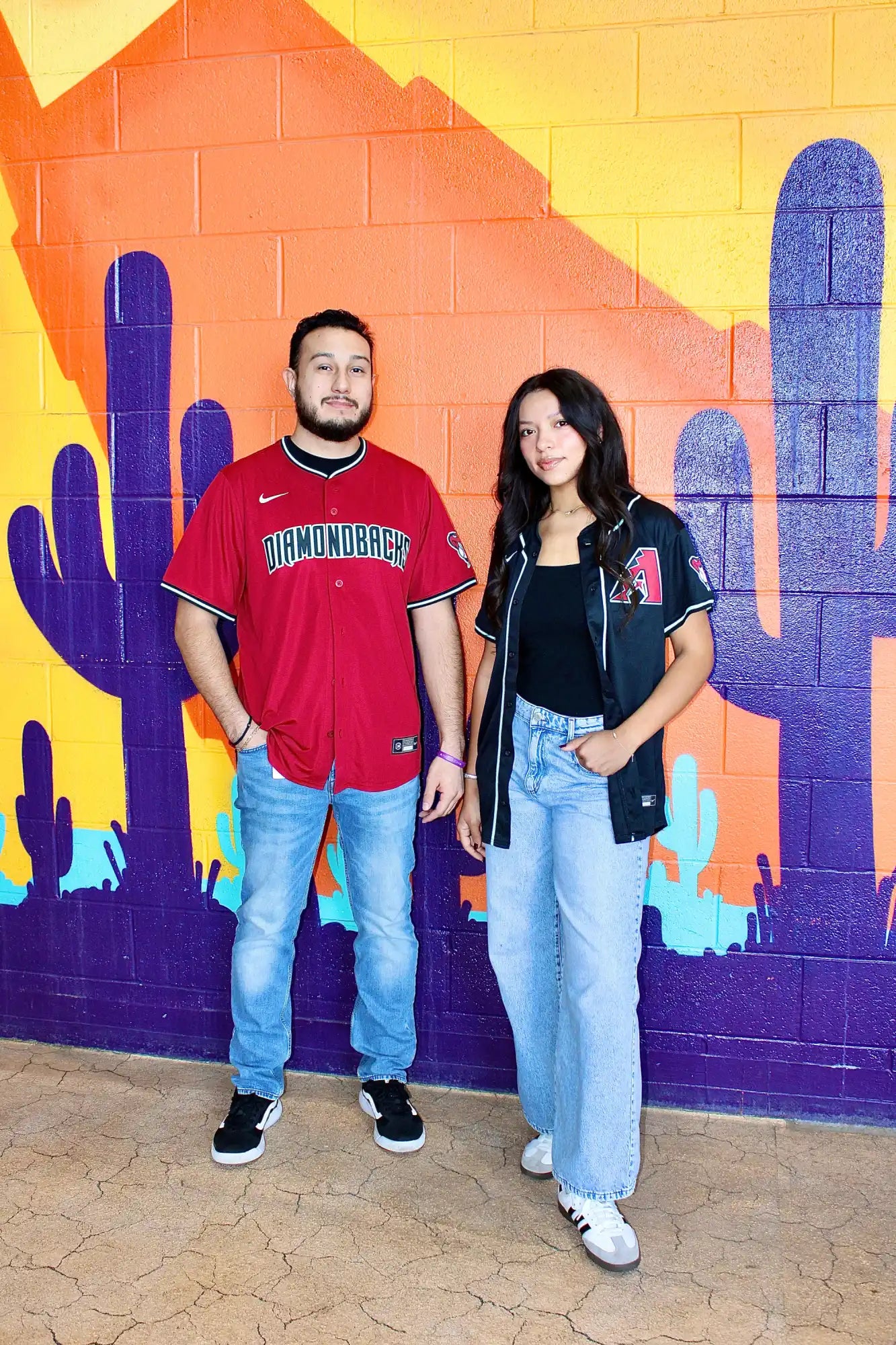 Two people standing together against a colorful desert-themed mural.
